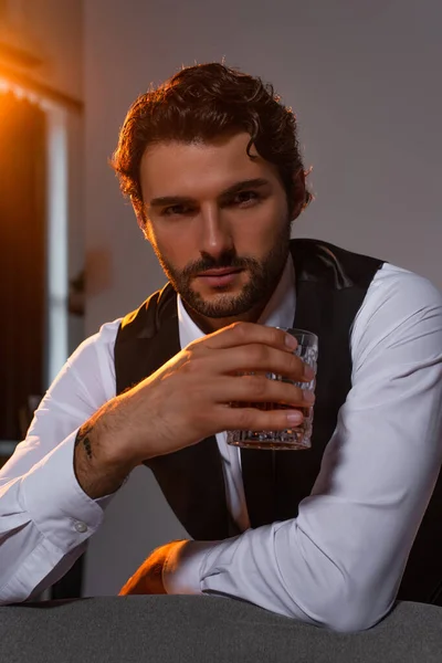 Homem de negócios elegante com vidro de uísque olhando para a câmera em fundo cinza — Fotografia de Stock
