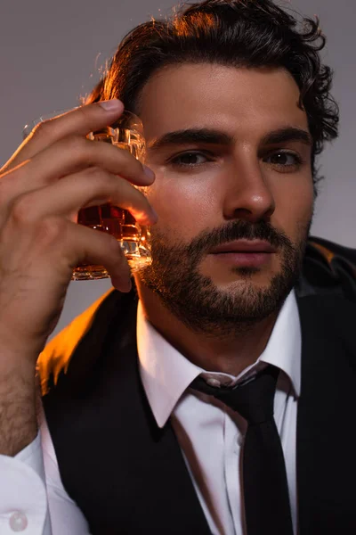 Vue rapprochée de brune homme avec verre de whisky regardant caméra isolée sur gris — Photo de stock