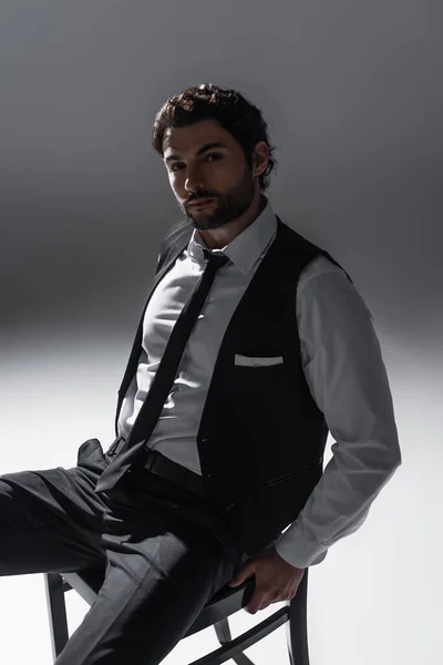 Brunette man in elegant formal wear looking at camera while sitting on grey — Stock Photo