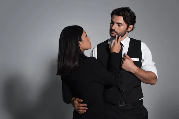 Sensual asiático mujer tocando cara de elegante hombre en gris fondo - foto de stock