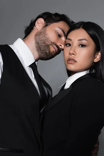 Sensual asian woman looking at camera while brunette man seducing her isolated on grey — Stock Photo