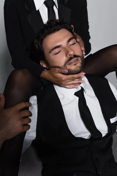 Passionate woman in black tights seducing elegant man sitting with closed eyes on grey background — Stock Photo