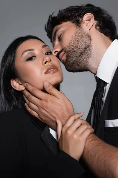 Elegant man seducing passionate asian woman looking at camera isolated on grey — Stock Photo