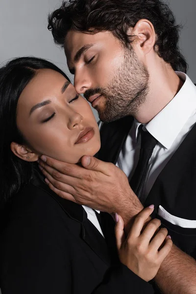 Elegant man kissing sensual asian woman isolated on grey — Stock Photo