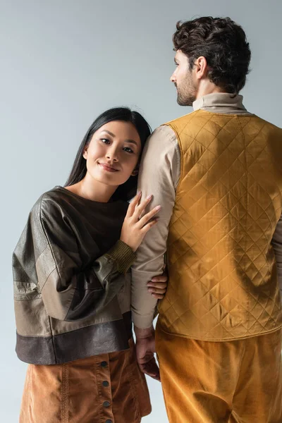 Mujer asiática feliz en jersey de cuero apoyado en el hombre en chaleco amarillo aislado en gris — Stock Photo