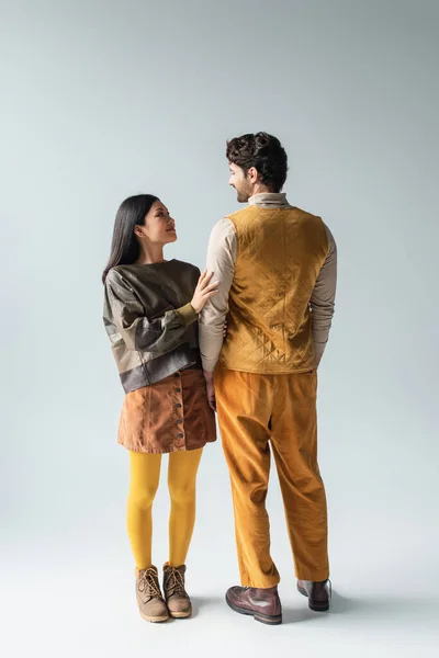 Vista posteriore dell'uomo in giubbotto giallo e pantaloni vicino sorridente donna asiatica sul grigio — Foto stock