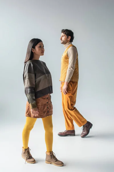 Full length view of asian woman and brunette man in stylish clothes walking on grey — Fotografia de Stock
