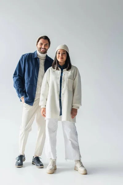 Vue pleine longueur du couple interracial en vêtements blancs et bleus à la mode sur fond gris — Photo de stock