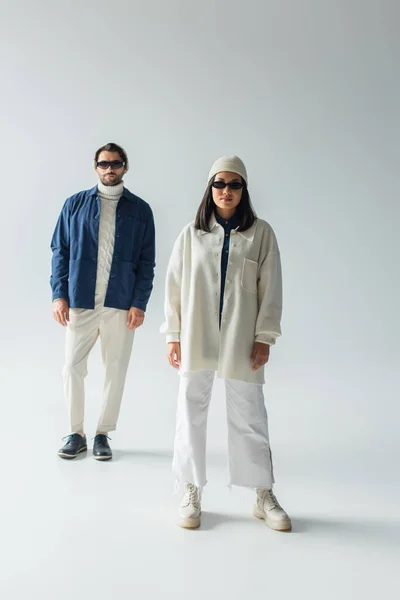 Full length view of interracial couple in white and blue clothes standing on grey — Stock Photo