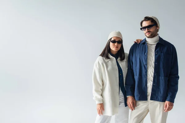 Trendy interracial Paar mit dunkler Sonnenbrille Blick auf Kamera isoliert auf grau — Stockfoto