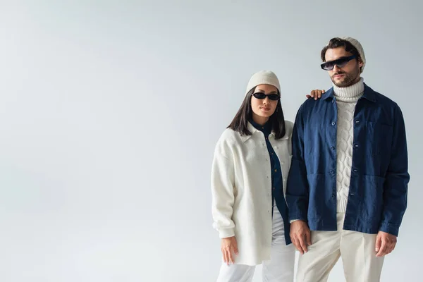 Trendy interracial couple in dark sunglasses looking at camera isolated on grey — Stock Photo