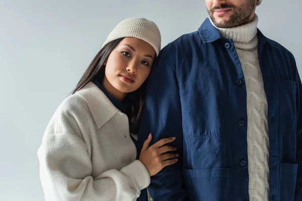 Jovem asiático mulher no beanie inclinado no homem no azul jaqueta isolado no cinza — Fotografia de Stock