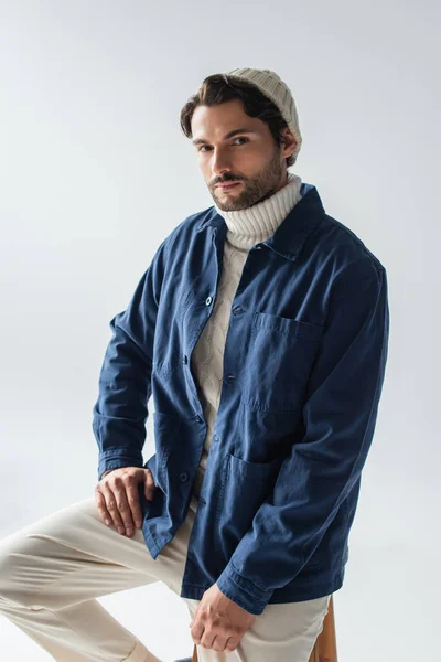 Hombre con estilo en chaqueta azul y gorro blanco mirando a la cámara aislada en gris - foto de stock