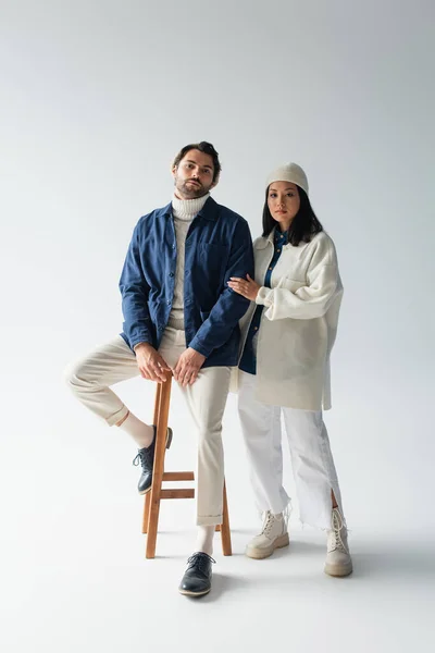 Hombre en azul chaqueta sentado en alto taburete limpio moda asiático mujer en gris - foto de stock