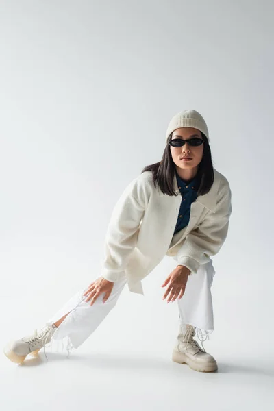 Full length view of asian woman posing in white clothes and dark sunglasses on grey — Stock Photo