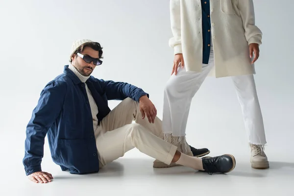 Homme élégant en veste bleue et lunettes de soleil sombres assis près de la femme sur gris — Photo de stock