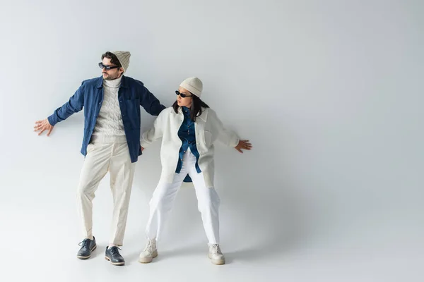 Full length view of interracial couple in trendy clothes and sunglasses posing on grey — Stock Photo