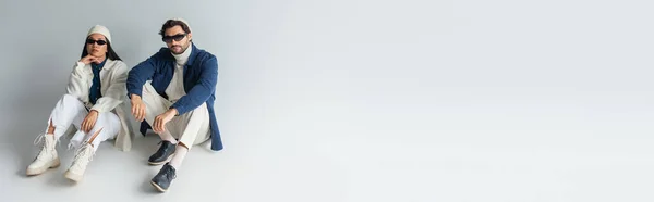 Високий кут зору модна багатоетнічна пара сидить на сірому, банер — стокове фото