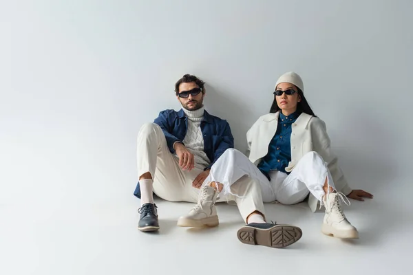 Vista completa de pareja interracial en ropa blanca y azul sentada en gris — Stock Photo