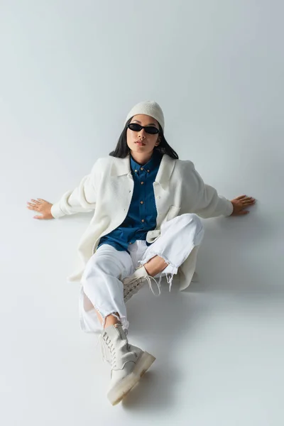 Alto ángulo vista de asiático mujer en blanco ropa y oscuro gafas de sol sentado en gris - foto de stock