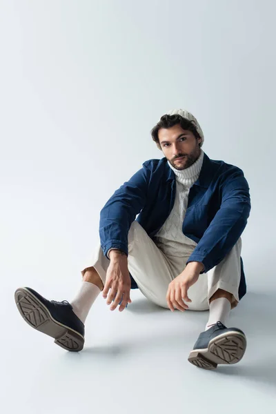 Full length view of brunette man in fashionable clothes sitting on grey — Stock Photo