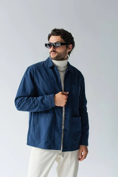 Uomo di tendenza in occhiali da sole scuri e giacca blu guardando altrove isolato sul grigio — Foto stock
