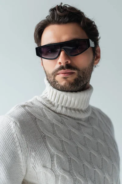 Trendy man in white sweater and dark sunglasses looking at camera isolated on grey — Stock Photo