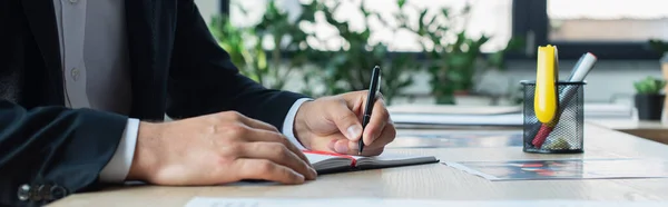 Vista recortada de la escritura del hombre de negocios en cuaderno en la oficina, bandera - foto de stock