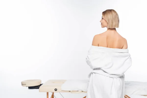 Side view of cheerful woman take off bathrobe near massage table on white — Stock Photo