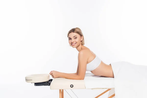 Alegre joven mujer en la parte superior de la cosecha acostado en la mesa de masaje en blanco — Stock Photo