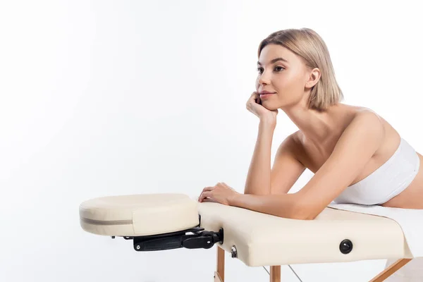 Jovem mulher satisfeita no topo da colheita deitado na mesa de massagem isolada no branco — Fotografia de Stock