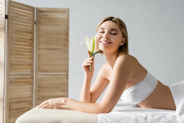 Mujer joven complacida con la flor acostada en la mesa de masaje - foto de stock