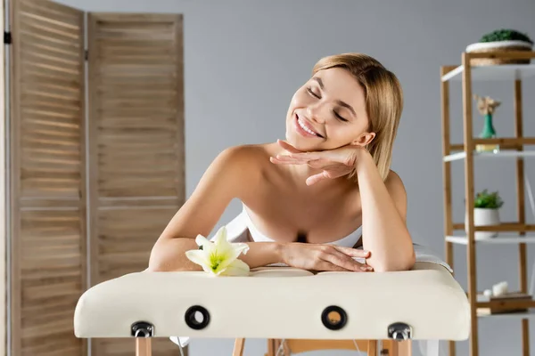 Joyeuse jeune femme allongée sur une table de massage près de la fleur — Photo de stock