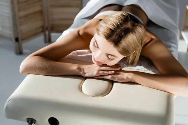 Visão de alto ângulo da jovem mulher alegre deitada na mesa de massagem — Fotografia de Stock