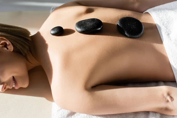 Vue recadrée de jeune femme heureuse recevant un massage aux pierres chaudes — Photo de stock