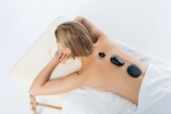 Vista de ángulo alto de la mujer joven que recibe masaje de piedra caliente aislado en blanco - foto de stock