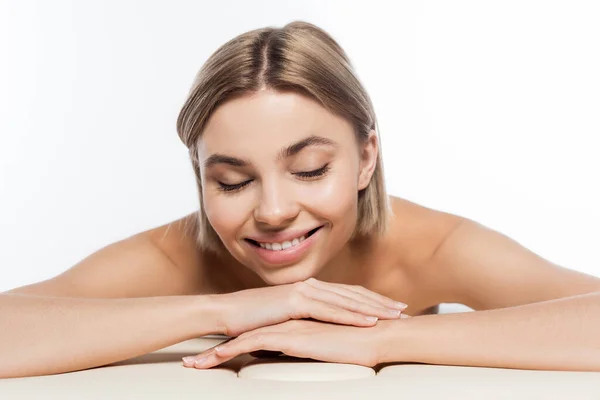 Cheerful blonde woman with bare shoulders lying on massage table isolated on white — Stock Photo