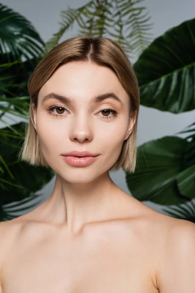 Jolie jeune femme aux épaules nues près des feuilles tropicales vertes sur fond gris — Photo de stock