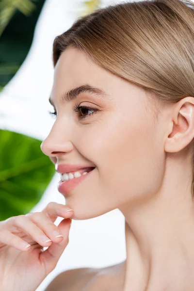 Primo piano di felice giovane donna con pelle perfetta vicino verde foglie tropicali su bianco — Foto stock