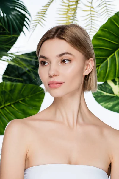 Young woman with perfect skin looking away near green palm leaves on white — Stock Photo