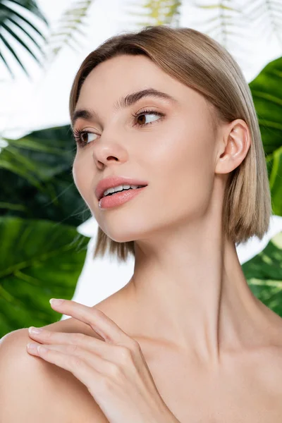 Bionda giovane donna con pelle perfetta guardando lontano vicino foglie di palma verde su bianco — Foto stock