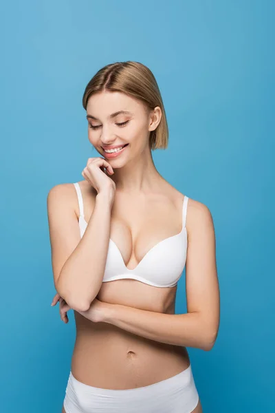 Slim young woman in white underwear smiling isolated on blue — Stock Photo