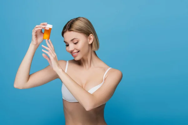 Freudige junge Frau in weißem BH mit Flasche mit Vitaminen auf blauem Grund — Stockfoto