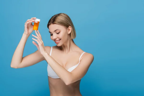 Jovem alegre em garrafa de sutiã branco segurando com vitaminas isoladas em azul — Fotografia de Stock