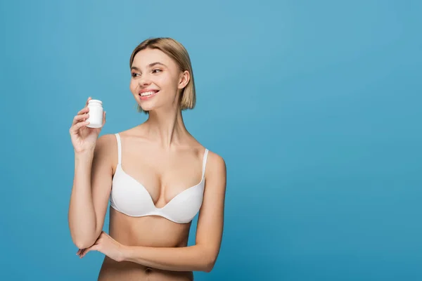 Modelo jovem feliz em garrafa de sutiã branco segurando com vitaminas isoladas em azul — Fotografia de Stock