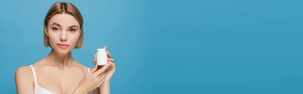 Blonde young woman in white bra holding bottle with vitamins isolated on blue, banner — Stock Photo