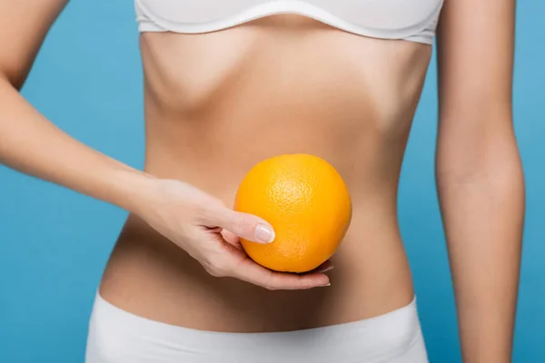 Vista cortada de jovem mulher em sutiã branco segurando laranja madura isolado em azul — Fotografia de Stock