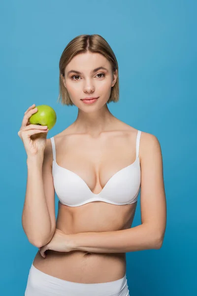 Blonde junge Frau in weißem BH mit reifem grünen Apfel auf blauem Hintergrund — Stockfoto