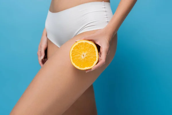 Cropped view of slim woman in white lingerie holding half of orange isolated on blue — Stock Photo