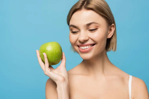 Fröhliche junge Frau hält reifen grünen Apfel isoliert auf blauem Grund — Stockfoto